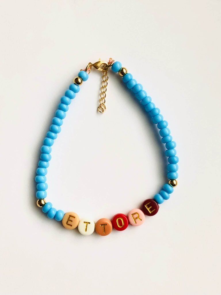 foto braccialetto di perline colorate celesti con scritto Ettore. Sfondo neutro