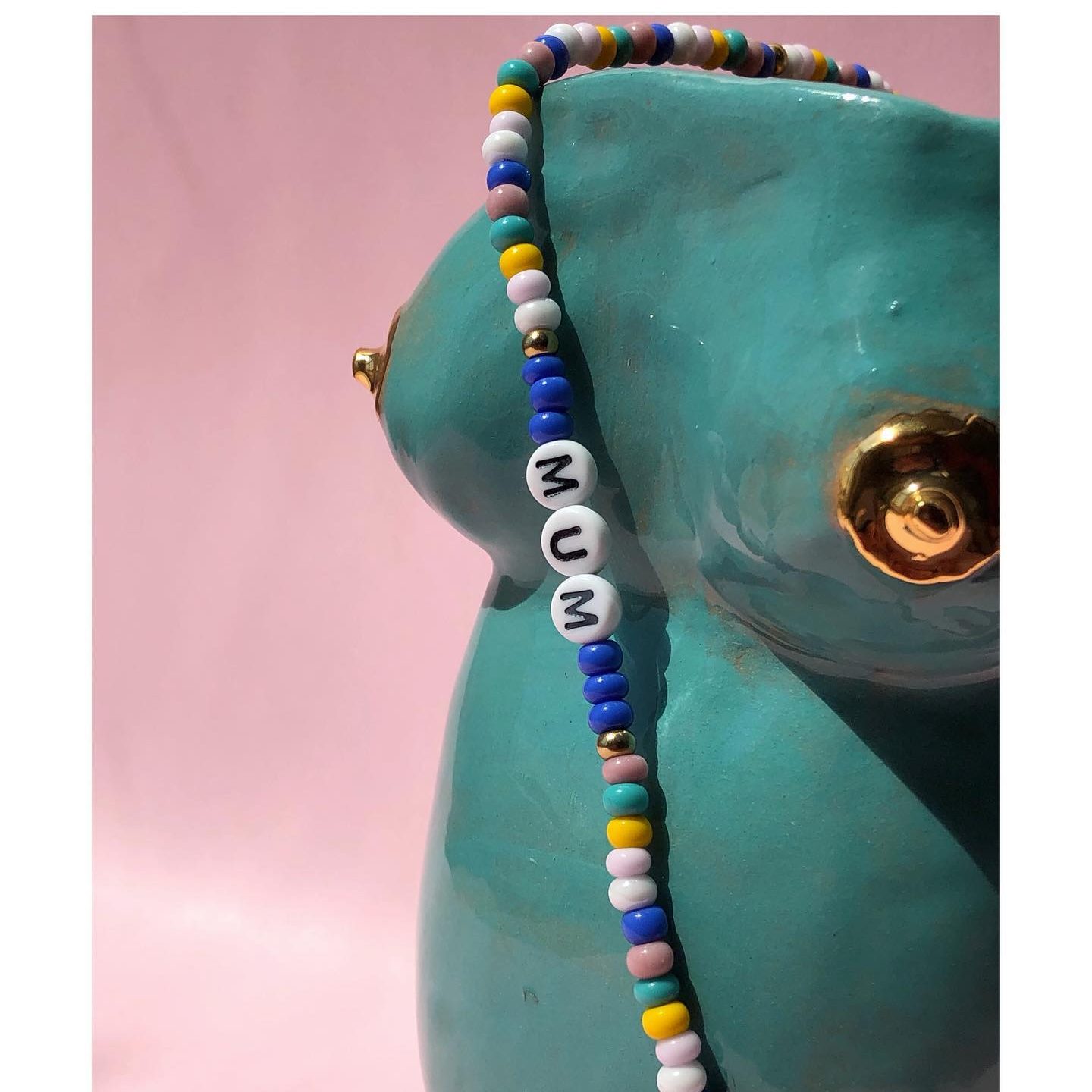 foto braccialetto perline colorate con personalizzato con scritto MUM appoggiato su scultura artigianale blu con dettagli oro