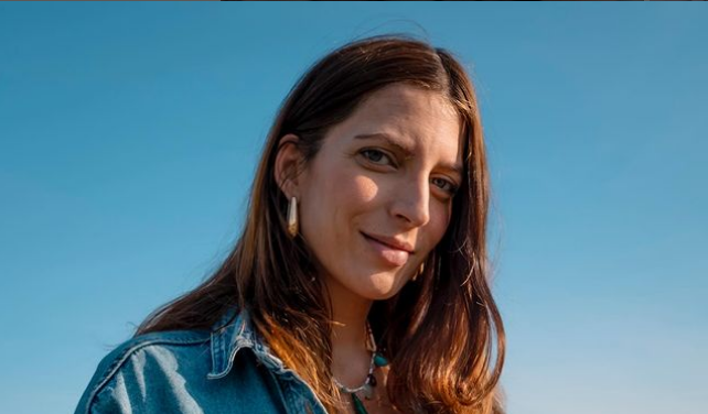 foto di ragazza in primo piano, Daniela Greco, con capelli lunghi marroni, occhi celesti, orecchini dorati big eyes creations e collana. Sondo celeste